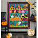 The completed Spooktacular Night Out quilt in cheerful Halloween colors, hung on a paneled wall beside coordinating festive decor like jack-o-lanterns and bats. A yellow banner in the upper right hand corner reads 