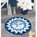 The completed Point of View Folded Star Table Topper colored in wintry blue, white, and navy fabrics from the Father Christmas collection by Northcott Fabrics, staged on a rustic gray wooden table and staged with sparkling silver tree candles and a bouquet of white poinsettias.
