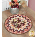 The completed Point of View Folded Star Table Topper colored in warm autumn fabrics from the Rustle collection by Maywood Studio, staged on a rustic wooden table with coordinating flowers and wine glasses.