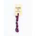 A skein of variegated purple embroidery floss, twisted and bundled, with a cream and black label featuring the brand name and color information.