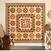 The completed Heartland quilt, a blended design of appliqué and patchwork colored in warm fabrics from the Toasted and Spice Market collections from Andover Fabrics. The project is hung on a light cream wall and staged with rustic farmhouse decor including a rocking chair, coordinating leaves, and a wagon wheel.
