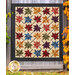 The Fluttering Leaves quilt, colored in colorful fabrics from the Flossie's Flowers collection by Henry Glass and hung on a gray wooden fence, framed by autumn trees.