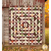 The completed Skip to My Lou Quilt colored in the warm prints of the Rustle collection, hung on a rustic wood-paneled barn in an autumn forest.