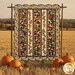 The completed Pumpkin Lane Quilt colored in rich orange, brown, blue, tan, and red fabrics from the Wheatland collection by Moda Fabrics, hung