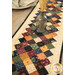 A close up on the patchwork of the table runner with a coordinating vase filled with wheat placed in the center.