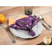 An angled shot of the napkin with the purple side faced out, staged on a gray table setting beside tossed Halloween decor.