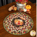 The completed Point of View Folded Star Table Topper colored in vibrant autumn-themed fabrics from the Gather With A Grateful Heart collection by Timeless Treasures Fabrics, staged on a dark wood table with coordinating fall decor.