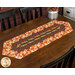 The Easy Striped Table Runner colored in vibrant autumn-themed fabrics from the Gather With A Grateful Heart collection by Timeless Treasures Fabrics, staged on a wooden table.