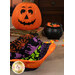 A completed Bowl Cozy colored in black, green, purple, and orange fabrics from the Tonga Haunted Batiks collection, staged on a wooden table with candy corn and a decorative jack-o'-lantern.