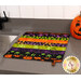 The completed Dry Ideas dish drying mat colored in black, green, purple, and orange fabrics from the Tonga Haunted Batiks collection, staged on a kitchen countertop beside a decorative jack-o'-lantern.