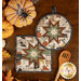 The two completed cream Folded Star Hot Pads, one round and one square, slightly overlapping each other and staged on a wooden table with coordinating pumpkin and Halloween décor.