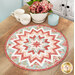 The completed Folded Star Table Topper, colored in pink, blue, and white fabrics from the Muse collection, staged on a wooden table with coordinating teacups and flowers.