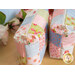 A top view of two finished mini-charm bags with hanging charms and patchwork design made from blue, pink, green, and white fabric from the Memory Lane collection by Moda, on a wooden table with coordinating summer decor in the background.