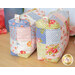 Two finished mini-charm bags with hanging charms and patchwork design made from blue, pink, green, and white fabric from the Memory Lane collection by Moda, on a wooden table with coordinating summer decor in the background.