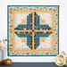 The completed Log Cabin Wall Hanging colored in aqua, navy blue, cream, and orange fabrics, hung on a white paneled wall and staged with coordinating autumn decor.