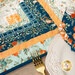 A super close up on the runner, demonstrating fabric colors and print details as well as top quilting effects. A coordinating tableware set peeks into frame from the lower right corner.