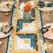 A top down shot of the topper staged on a wooden kitchen table and complementary table settings. A galvanized nickel can of coordinating flowers sits in the center of the project.