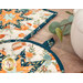 A stylized close up on the two hot pads on a wooden table. Leaves and a ceramic teapot peek into frame from the right side.