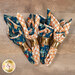 The four cloth napkins in floral and plaid fabrics from the I Love Fall Most of All collection, tied with gold rings, on a wooden tabletop.