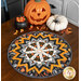The completed Point of View Kaleidoscope Folded Star Table Topper colored in black, orange, gray, and cream Halloween fabrics from the The Boo Crew collection by Northcott Fabrics, staged on a wooden table and staged with coordinating pumpkins, candy corn, and other Halloween décor.