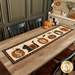 The completed Spooky Kitty Table Runner, colored in floral and primitive prints from the Cheddar and Coal III collection, staged on a wooden table with coordinating autumn decor.