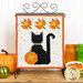 Halloween themed table top banner with orange leaves, a pumpkin, and a black cat on a white background, hung on a display hanger and staged with coordinating decor.