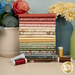 A stack of the fabrics included in the Kathleen's Story Fat Quarter Bundle, with vases and flowers and thread.