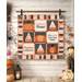 The completed Candy Harvesting Time Quilt, colored in orange, pink, white, and black fabrics from the Hey Pumpkin collection by Riley Blake Designs, hung on a white wood paneled wall and staged with coordinating Halloween decor.