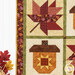 A close up on the side of the project, demonstrating fabric colors on the leaf and acorn blocks as well as the borders and binding. Coordinating decorative leaves peek into frame from the lower left corner.