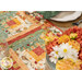 A shot of the log cabin patchwork of the runner, demonstrating vibrant fabric colors and prints as well as top quilting details; coordinating flowers and table ware peek into frame.