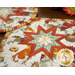 A stylized close up on the two hot pads on a wooden table. Leaves and coordinating florals peek into frame from the edges.