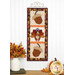 The finished Foundation Paper Piecing Series 3 November project colored in neutral browns and oranges, hung on a golden craft hanger on a white paneled wall above coordinating autumnal decor set on a wooden tabletop.
