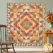 The completed Harvest Blooms Quilt colored in autumn-themed prints from the Harvest Blooms collection by Wilmington prints, hung on a pale sage green wall and staged with a rocking chair and coordinating decor.