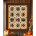 The completed Woven Dreams quilt colored in warm brown, gold, and cream primitive fabrics from the Wheatland collection by Moda Fabrics, hung on a wooden wall and staged with pumpkins and autumnal décor.