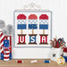 The completed July spool, three popsicles in patriotic colors, hung on a craft hanger and staged above a wooden table with coordinating spools and decor.