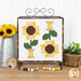 The completed August spool, two yellow, brown, and green spools, hung on a craft holder and staged on a wooden table with coordinating spools and decor.