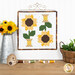The completed August spool, two yellow, brown, and green spools, hung on a craft hanger and staged above a wooden table with coordinating spools and decor.