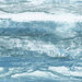 Fabric with a rough textured print in shades of deep teal, ice blue, and white which resembles waves and rugged coastline