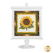 A finished and assembled version of the pedestal frame, painted white and displaying a yellow, brown, and green cross stitch project featuring a sunflower. 