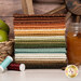 A stack of the fabrics included in the Cider Mill collection, with apples and cinnamon and a basket and a wagon wheel and a jar of cider and thread.