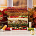 A stack of the fabrics included in the Harvest Beauty collection, with leaves and flowers and a jar and thread.