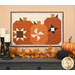 The completed Pumpkin Patch Trio kit colored in the rich fall colors of the Midnight Moon collection from Andover Fabrics, hung above a gray armoire set with coordinating fall décor.
