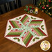The completed 60 Degree Diamond Table Topper, colored in white, red, green, and aqua fabrics from the Make it Merry collection from Marcus Fabrics, staged on a wooden table with coordinating holiday decor.