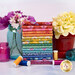 A stack of fabrics included in the Kipling Gardens collection with fuchsia, orange, mustard, teal, and blue fabrics with a bright floral theme.