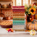 A stack of the fabrics included in the Baked with Love collection, with a kitchen and flowers and jars and a pumpkin and a pie and thread and leaves.