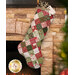 The completed Fast Fusible Patchwork Stocking colored in the Berry & Pine collection by Moda Fabrics, hung on a stone fireplace with Christmas decor and gifts peeking out of the top of the stocking.