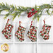 The four completed Fast Fusible Patchwork Stockings colored in the Berry & Pine collection from Moda Fabrics, hung on a string by clothespins in front of white wooden decor with Christmas garland at the top.