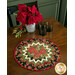 The completed Point of View Folded Star Table Topper colored in black, red, and green fabrics from the Joyful collection. The topper is staged on a wooden table with coordinating poinsettias and black glassware.
