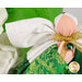 Detail shot of the angel, highlighting the metallic effect of the wings and the angel's metallic gold bow featuring a vivid green charm that resembles an emerald in a golden setting.