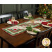 The completed table runner made with log cabin blocks of red, green, mint, and white fabrics from the Mistletoe & Holly collection, laying in the center of a wooden dining table with four place settings at each seat with matching cloth napkins.